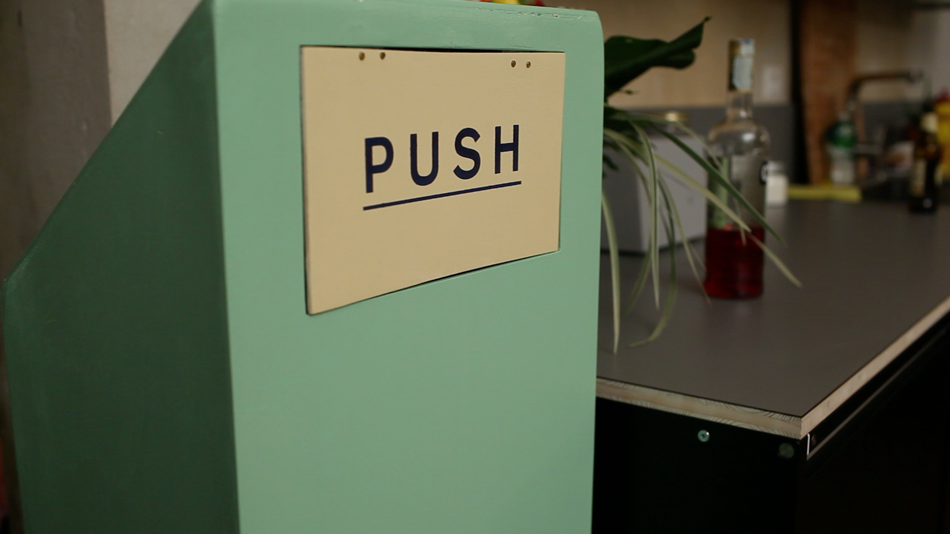 Close up picture of a teal trash can with a push sign swinging door — this trash can grows!